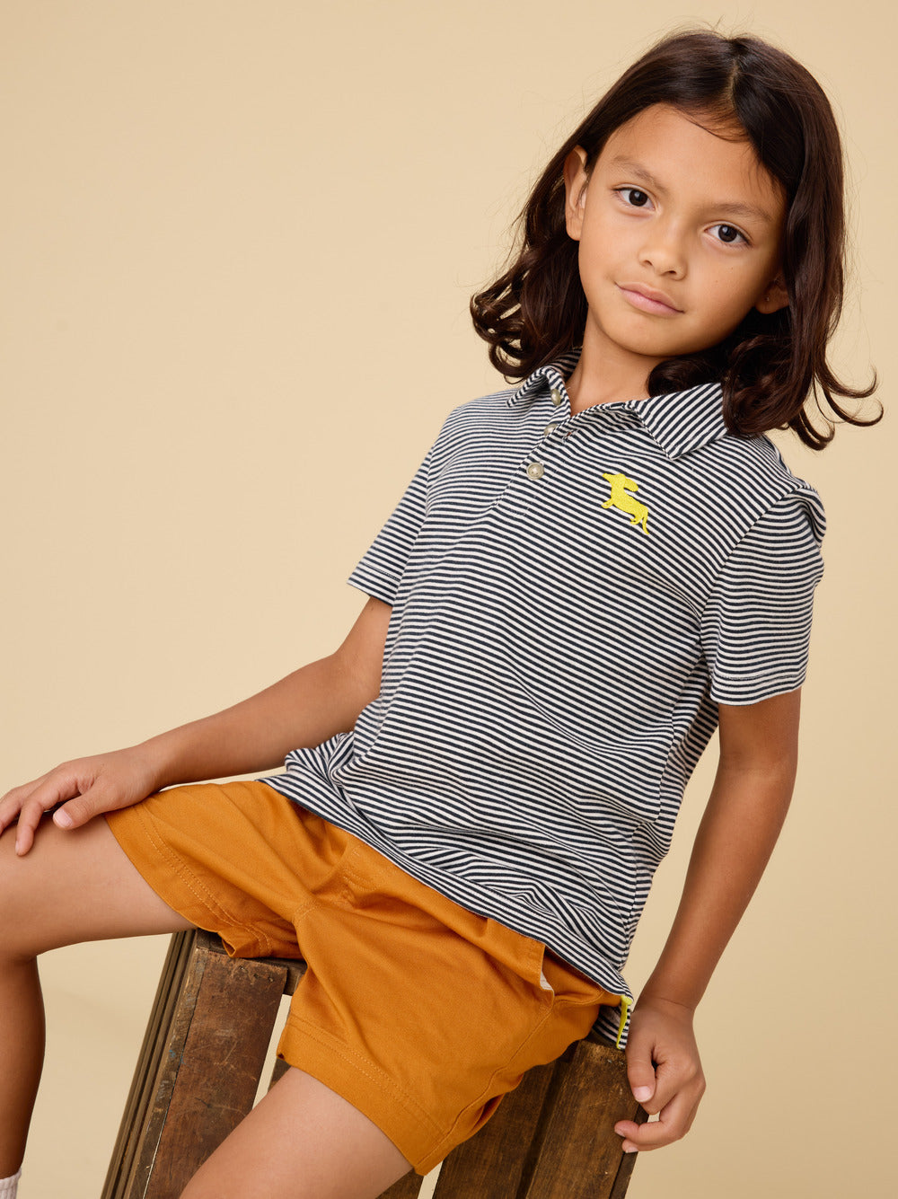 Child wearing a striped shirt and orange shorts on a beige background