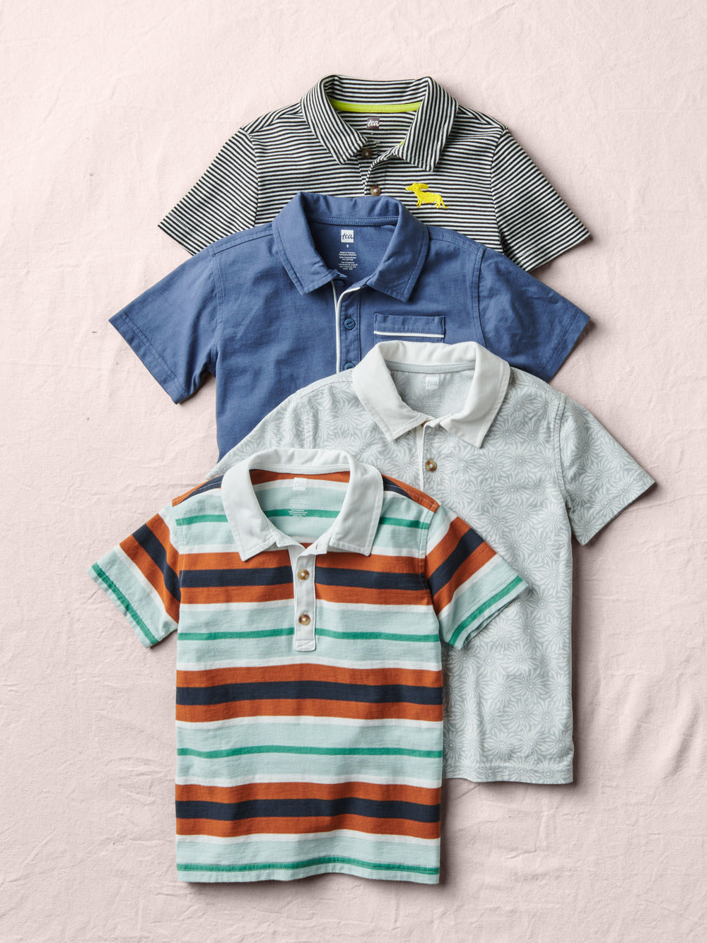 Four children's polo shirts in different colors and patterns on a light pink background