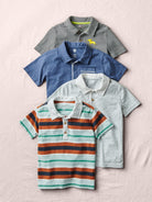 Four children's polo shirts in different colors and patterns on a light pink background