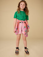 Young girl wearing a green top and pink shorts with a floral pattern on a beige background