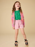 Young girl in a green shirt and pink shorts with a colorful jacket on a beige background