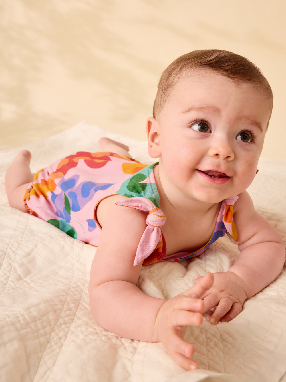 Baby wearing colorful pants lying on a beige blanket