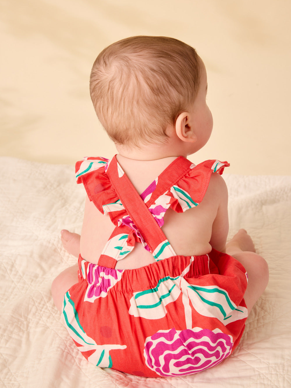 Baby wearing a colorful romper with ruffles on a beige background
