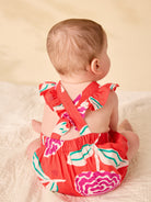 Baby wearing a colorful romper with ruffles on a beige background
