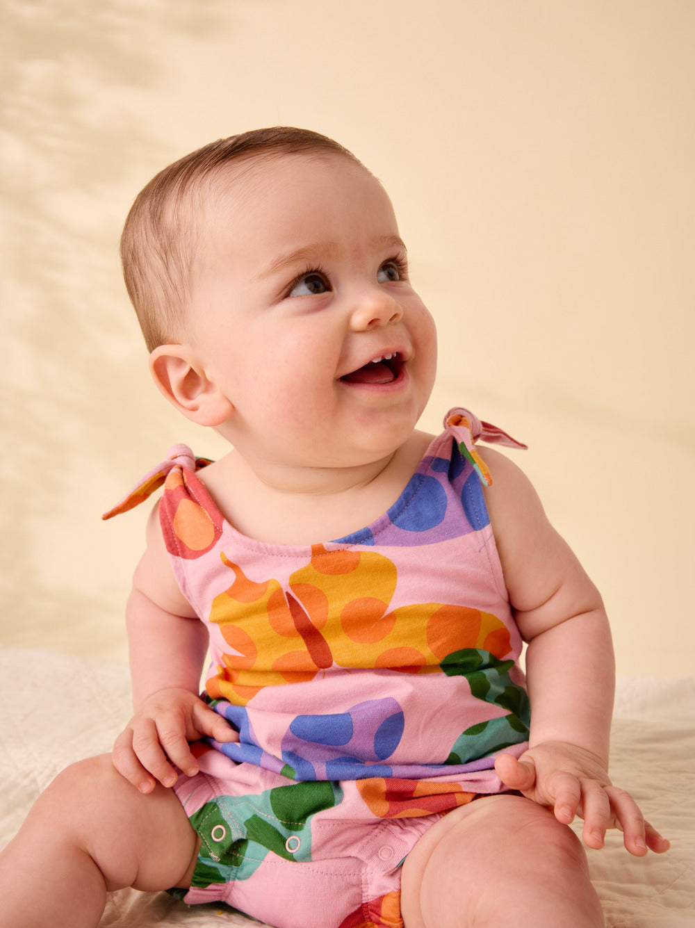 Baby wearing a colorful onesie against a beige background