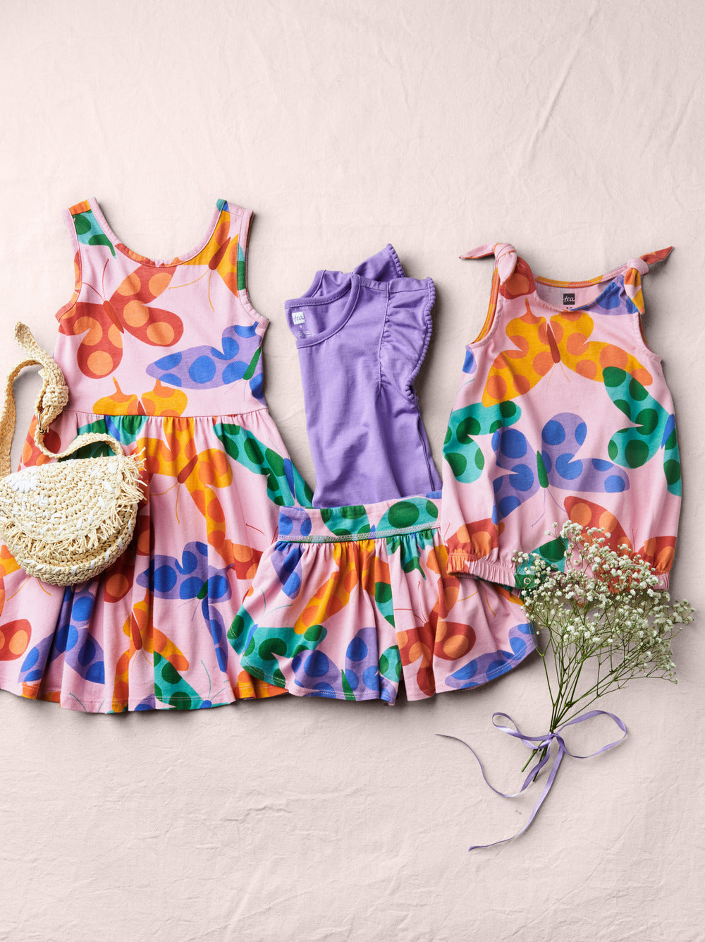 Two colorful floral dresses on a light background with a small bag and flowers.