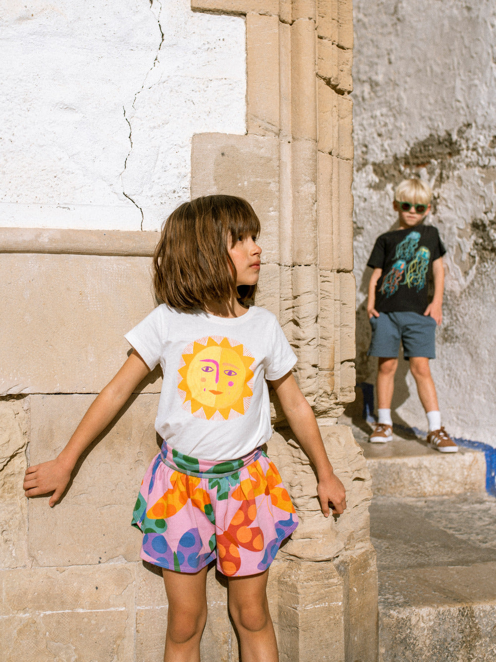 Two children in colorful clothing standing in front of stone architectural ruins.