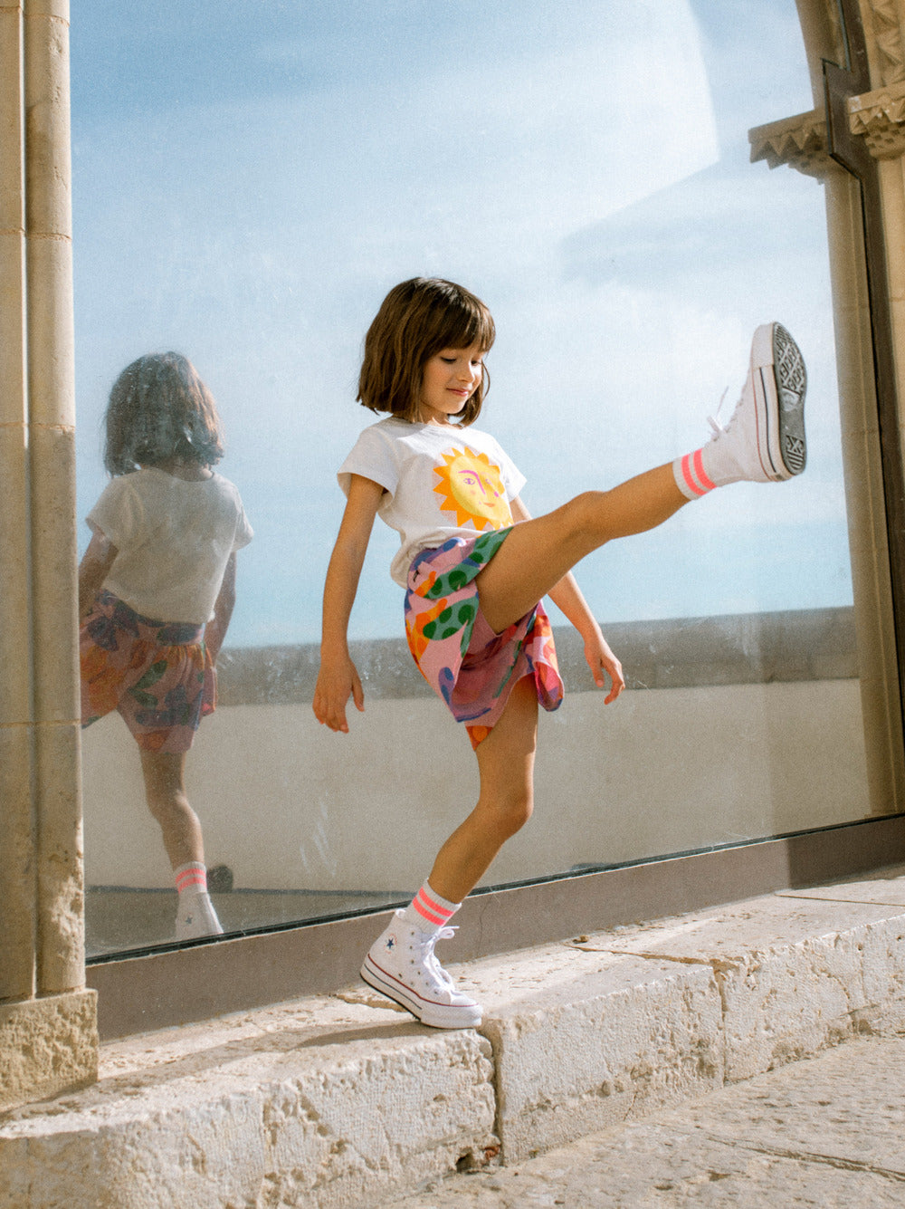 Child kicking a shoe on a stone ledge with a clear sky and reflection in the background
