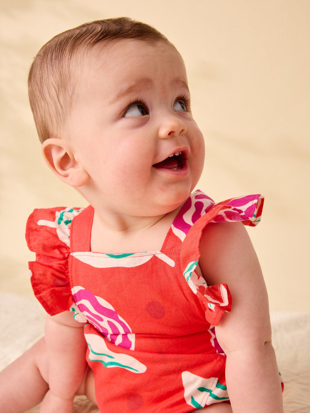 Baby wearing a red floral dress against a beige background