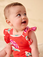 Baby wearing a red floral dress against a beige background