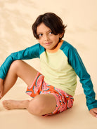 Child wearing a colorful shirt and shorts sitting on a beige surface