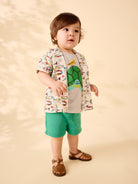 Child wearing a colorful shirt with animal prints and green shorts on a beige background