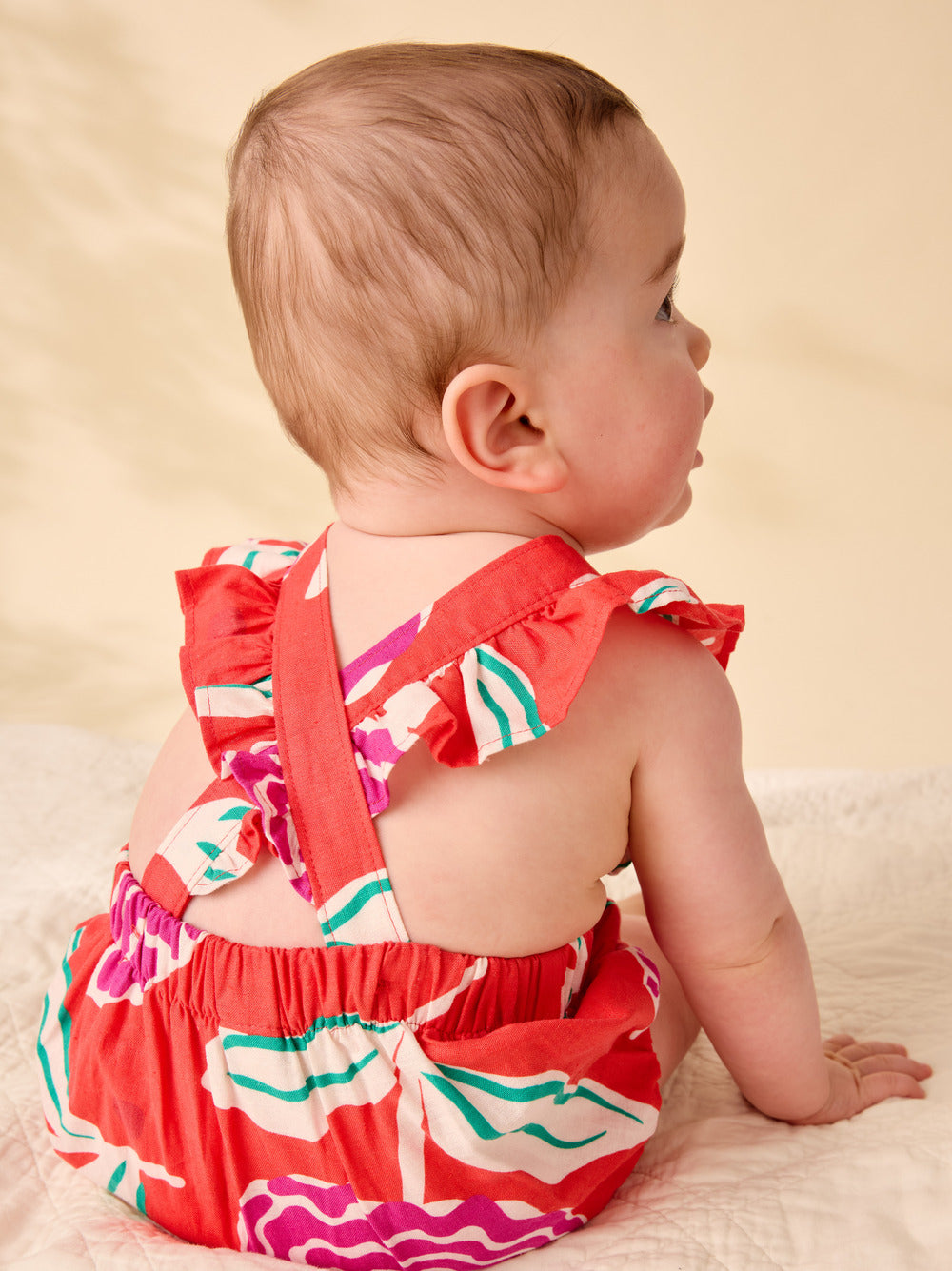 Baby wearing a colorful dress sitting on a beige surface