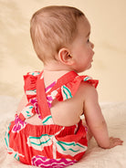 Baby wearing a colorful dress sitting on a beige surface