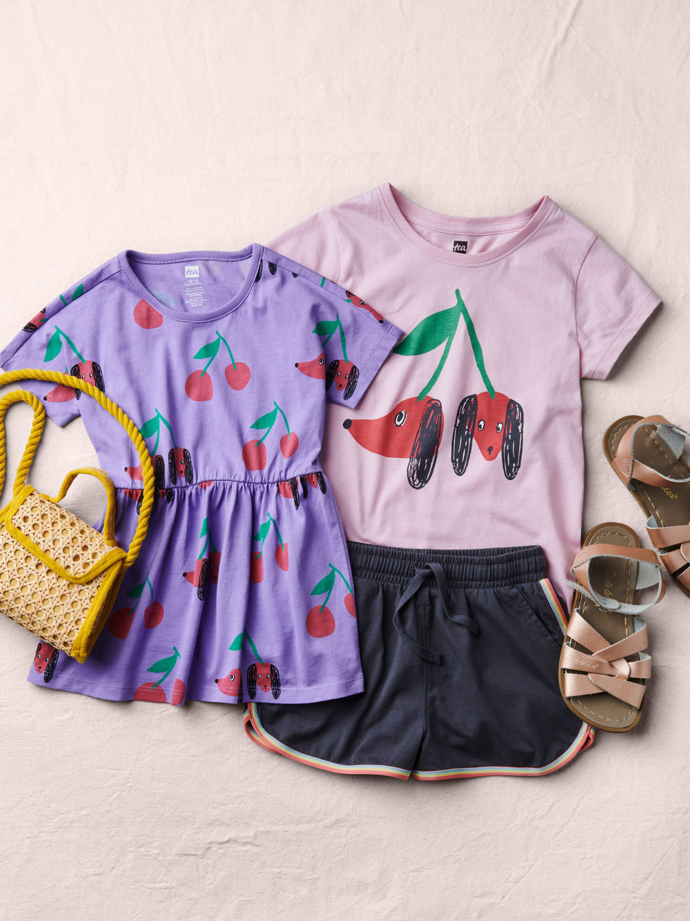 Children's clothing set with cherry-themed shirts and shorts on a light background