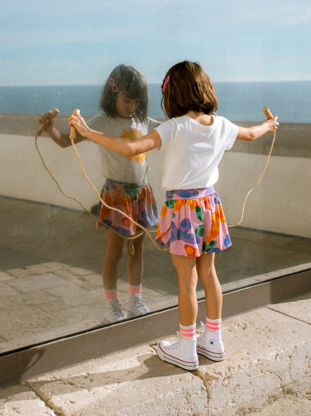 Young girl playing with a jump rope in front of a mirror reflecting the ocean.