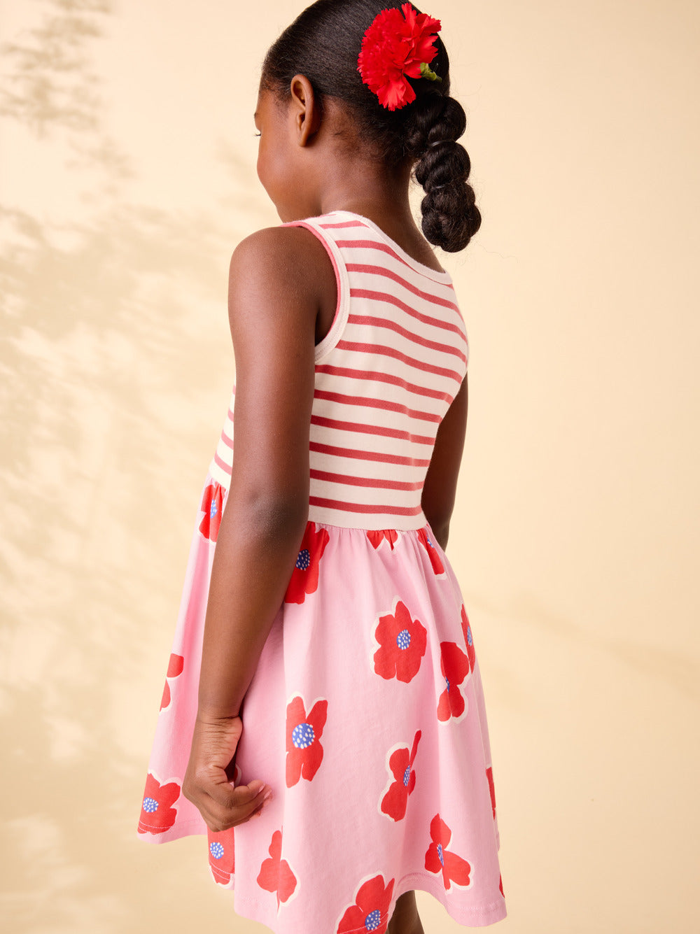 Young girl wearing a red and white striped dress with floral patterns on a beige background