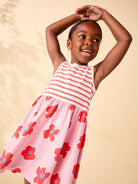 Young girl wearing a pink dress with red floral patterns on a beige background