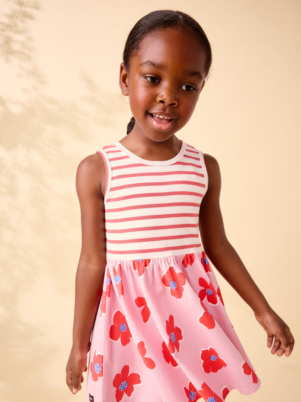 Young girl wearing a pink and white striped dress with floral pattern on a beige background