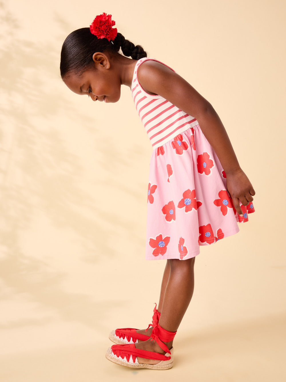 Young girl wearing a pink floral dress with red shoes on a beige background