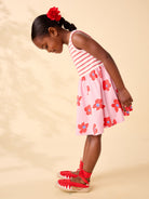 Young girl wearing a pink floral dress with red shoes on a beige background