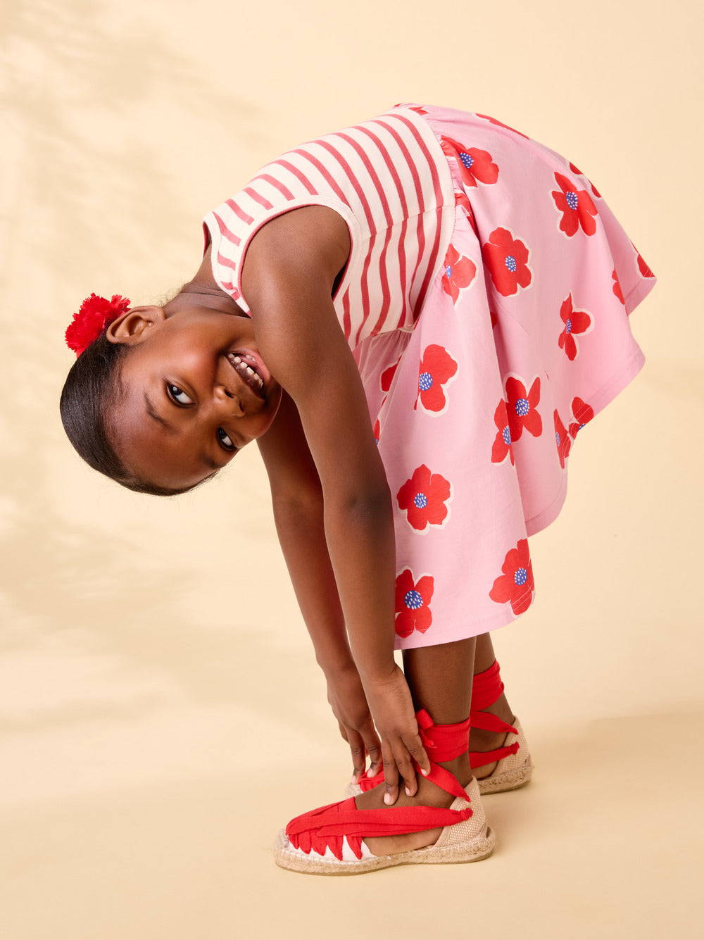 Young girl wearing a pink floral dress with red shoes on a beige background