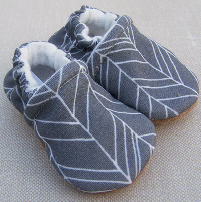 Pair of gray baby shoes with white patterns on a light gray background