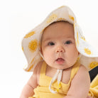 Baby wearing a yellow sun hat with sun patterns on a white background