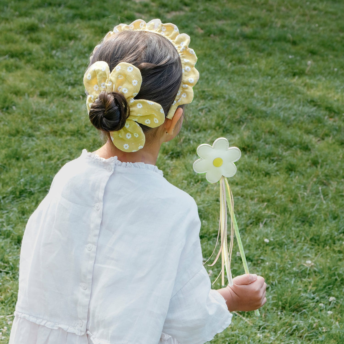 Child wearing a floral headband and holding a flower wand on grass