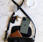 Black handbag with phone, wallet, keys, and car remote on a marble surface