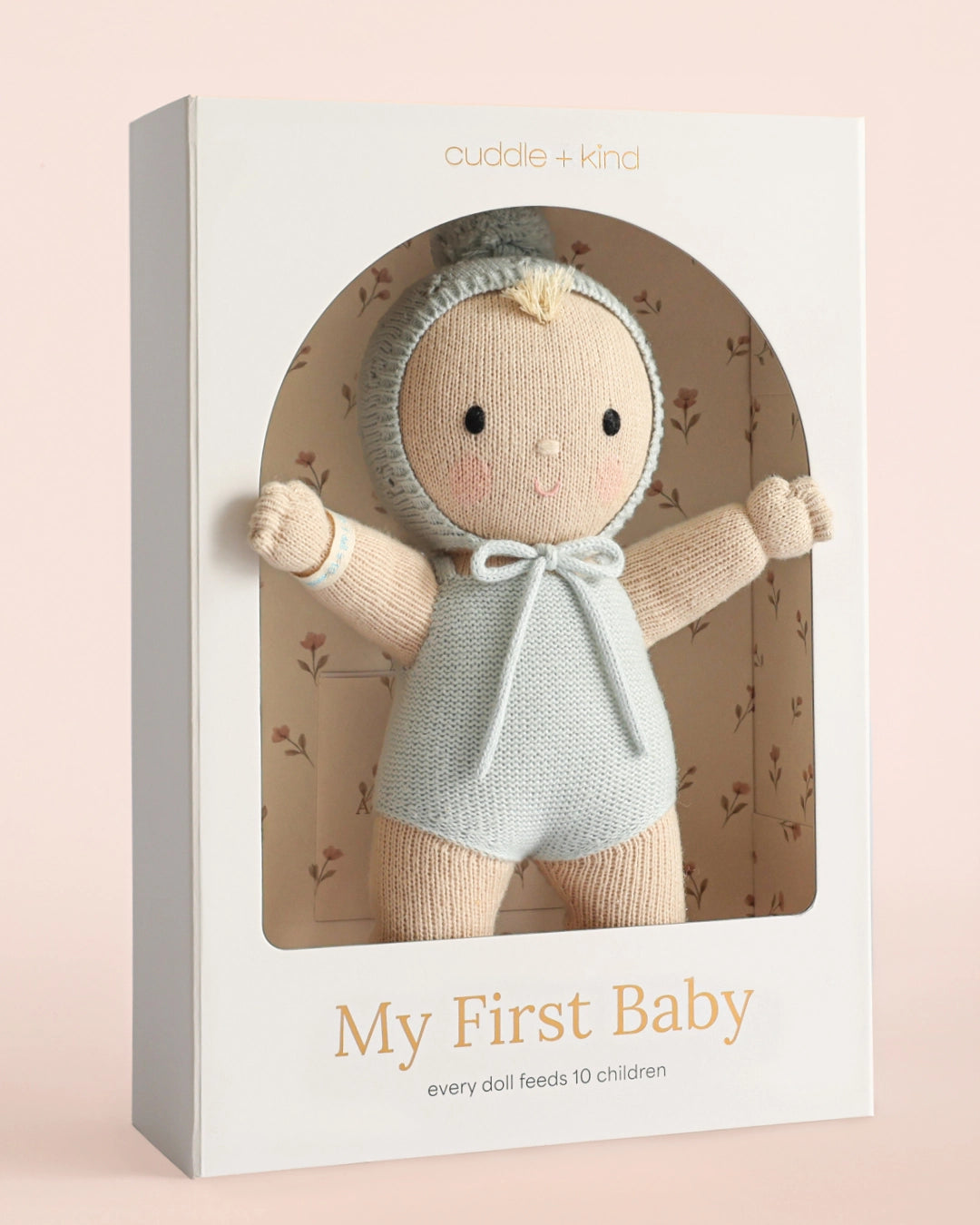 A knitted baby doll with a pale peach face and limbs, wearing a light blue knit bonnet with a pom-pom and a matching blue knitted romper, shown against a plain white background.