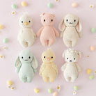 Six knitted toys in pastel colors on a light pink background with small colorful balls and flowers.