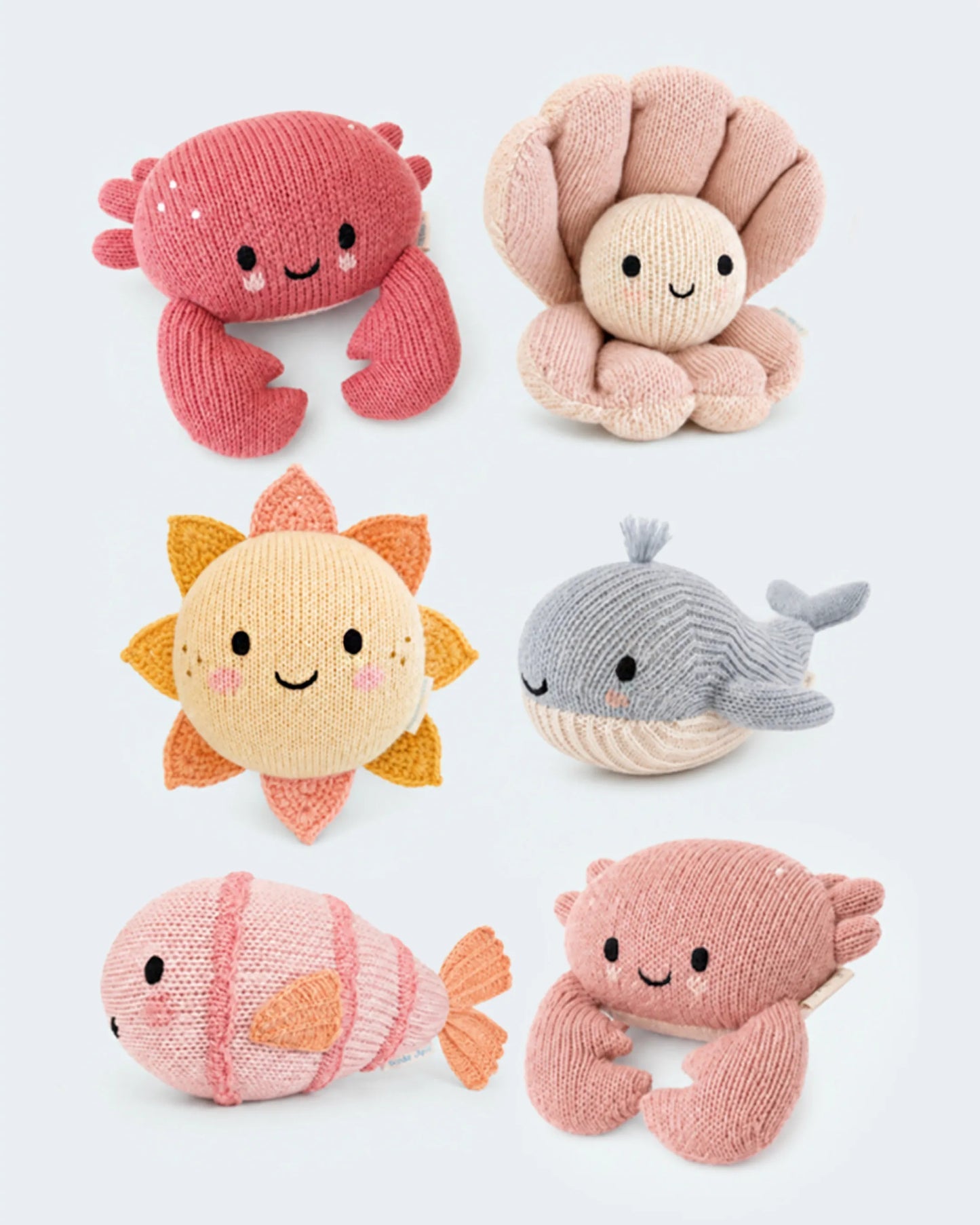 Six knitted plush toys arranged on a light gray background: a pink crab, a beige octopus, a yellow sun, a gray whale, a pink fish, and a pink crab.