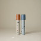 Two Mushie paper kaleidoscopes standing vertically against a light background, featuring the Space and Dinosaurs pattern with blue and orange caps.