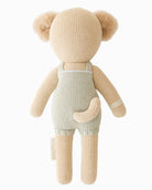 Knitted teddy bear wearing a light green romper on a white background