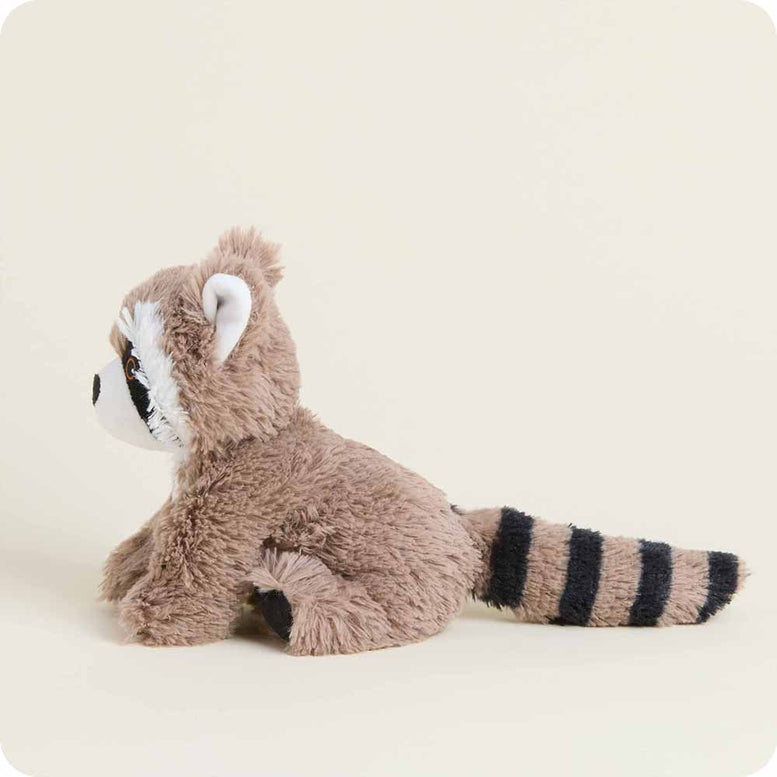 A Raccoon Junior plush toy by Warmies, featuring fuzzy brown fur, a white muzzle, black eye patches, and a striped tail, shown from the side in a sitting position.