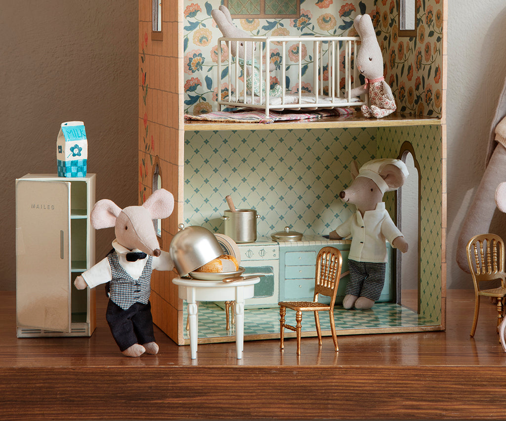 Miniature kitchen scene with toy mice and furniture in a dollhouse setting.