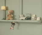 Decorative shelf with teddy bear, small bed, and lamp against a green wall