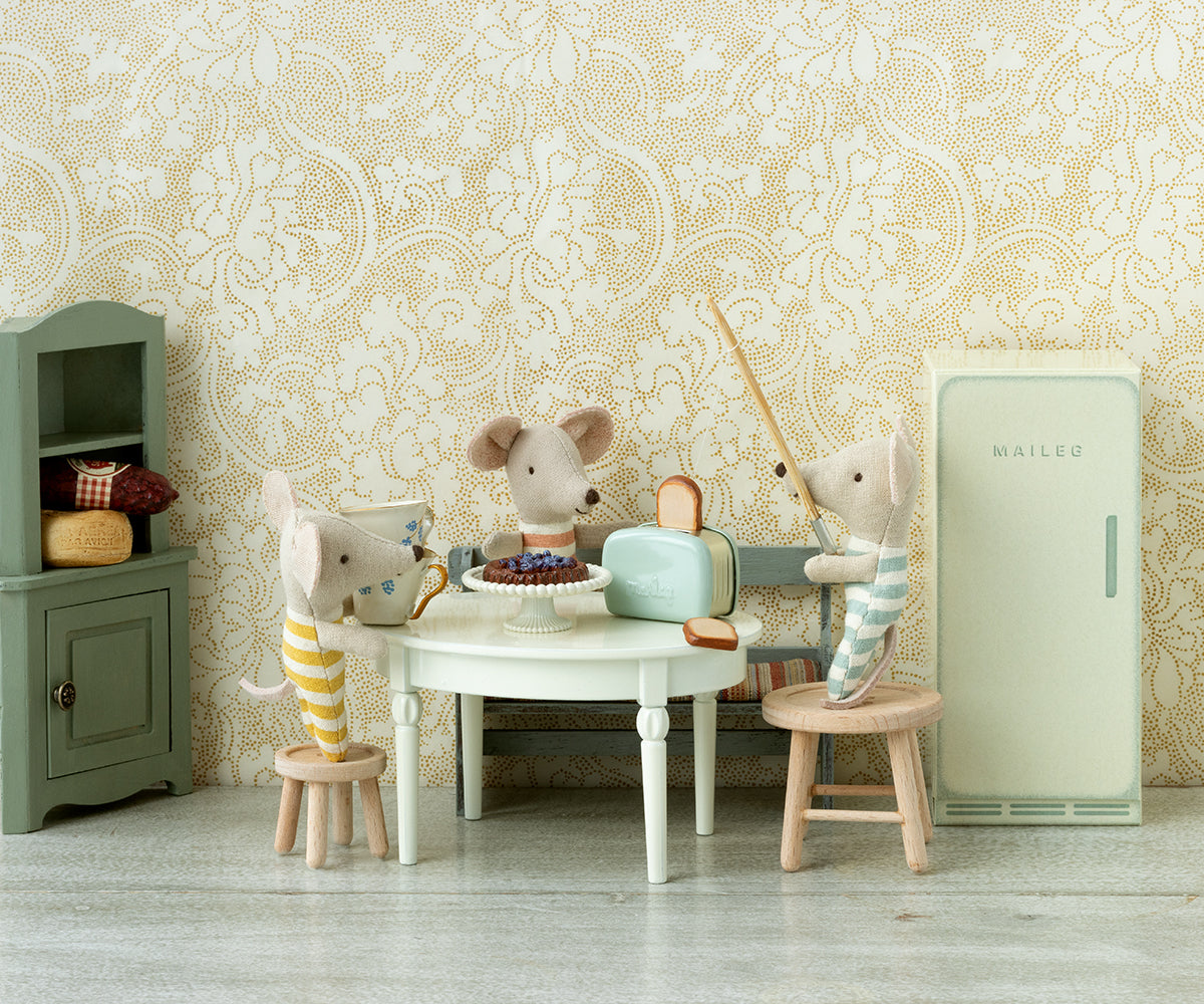 Miniature scene with toy mice around a table in a room with decorative wallpaper.