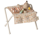 Maileg off-white miniature nursery changing table for baby mice, featuring metal folding legs, a polka-dot fabric changing pad, side pockets, a tiny rattle, and a baby lotion bottle.