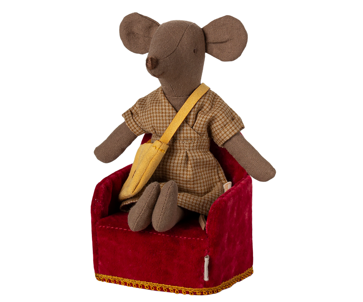 A Maileg mouse dressed in a plaid dress and yellow sash, sitting comfortably in a miniature red velvet armchair.