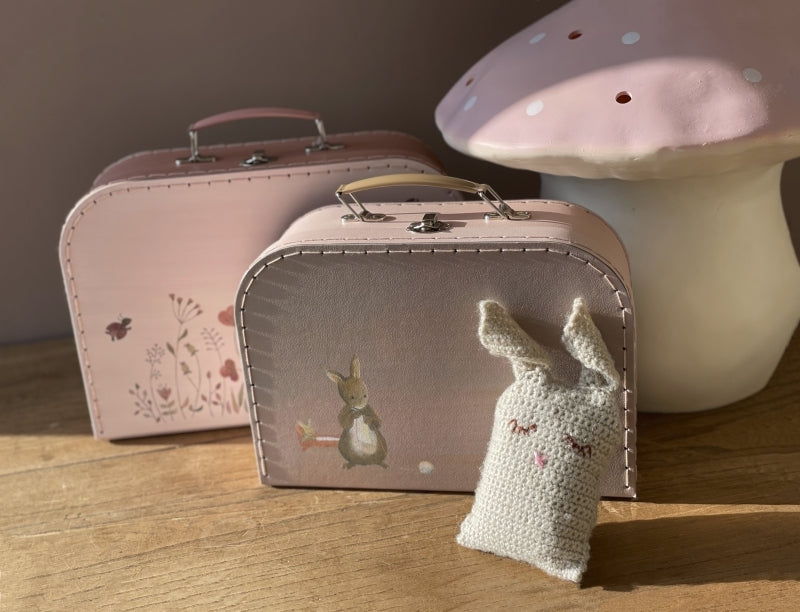 Small suitcase with rabbit design, pink suitcase, and knitted rabbit toy on a wooden surface.