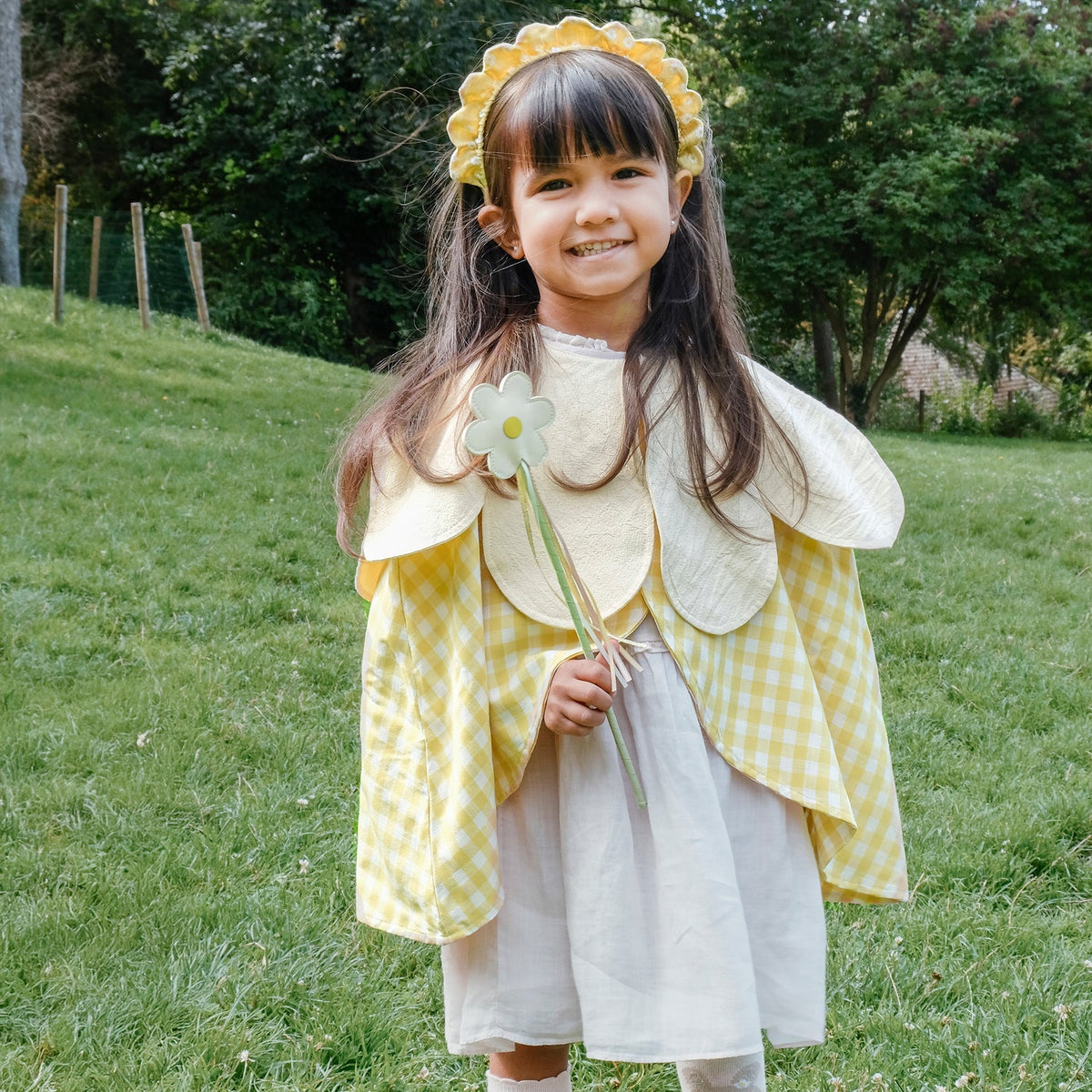 Child in a yellow dress with flower petals holding a flower in a grassy outdoor setting