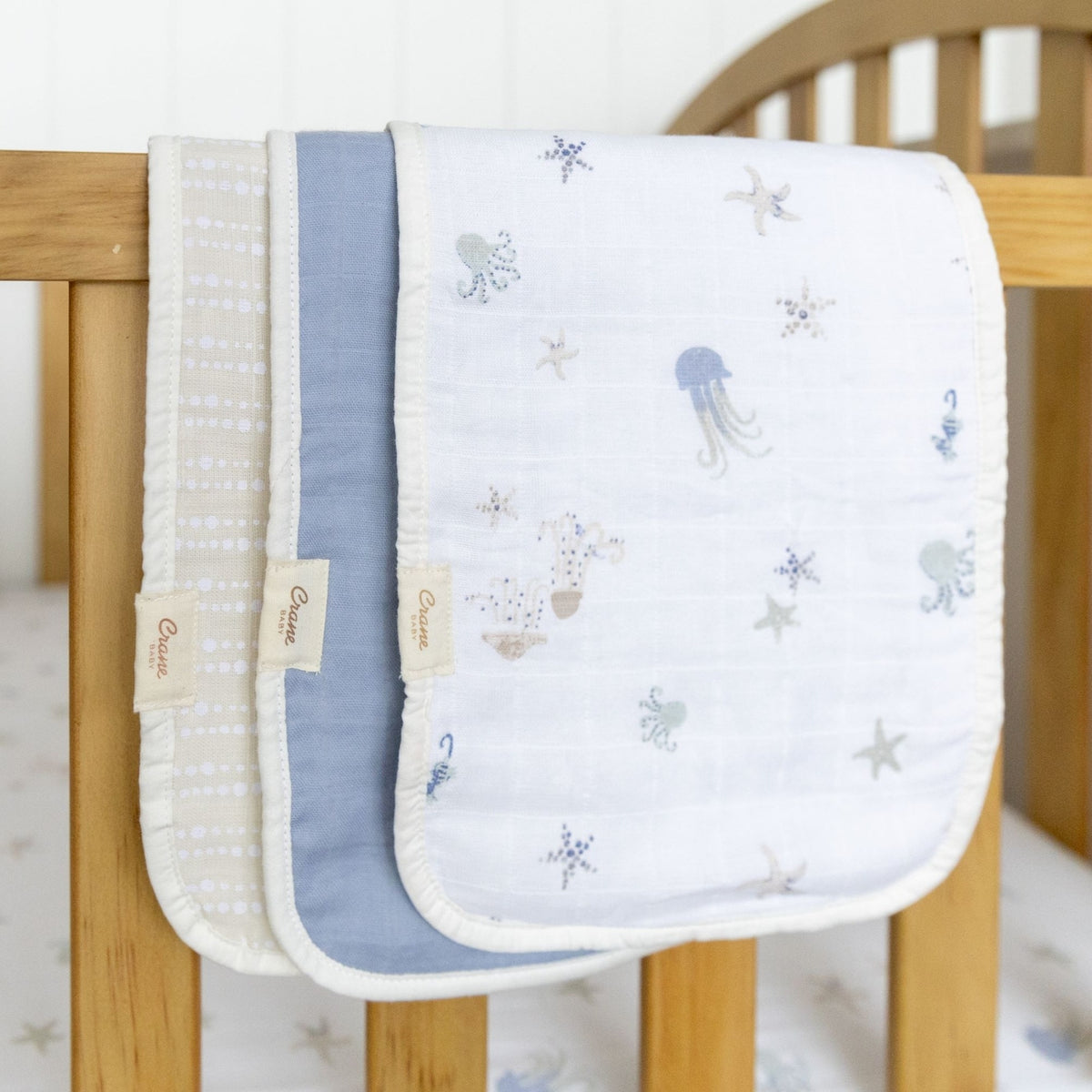 Two baby blankets with sea-themed embroidery on a wooden crib.