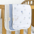 Two baby blankets with sea-themed embroidery on a wooden crib.