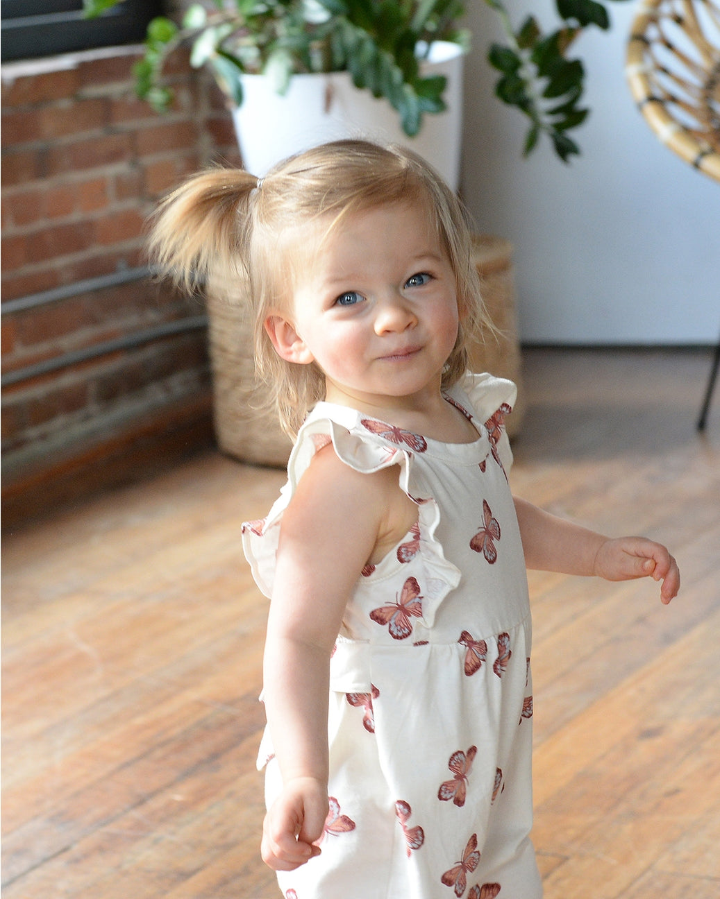 Young girl in a white dress with butterfly patterns standing on a wooden floor.