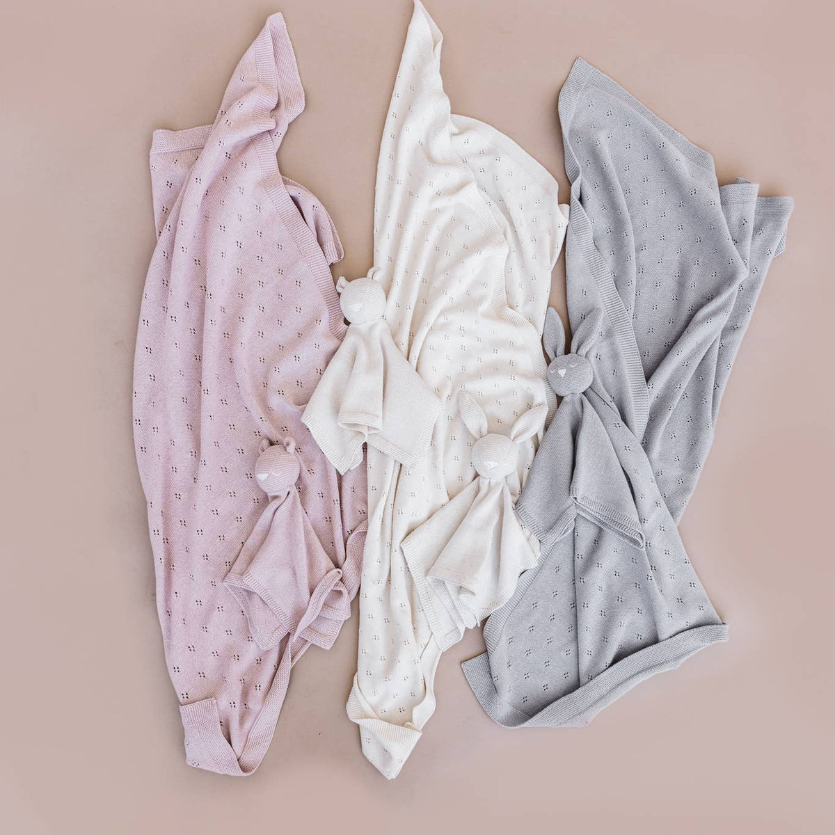 Three baby wraps in pink, white, and gray on a beige background