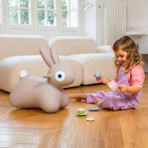 Child playing with a toy rabbit on a wooden floor in a living room.