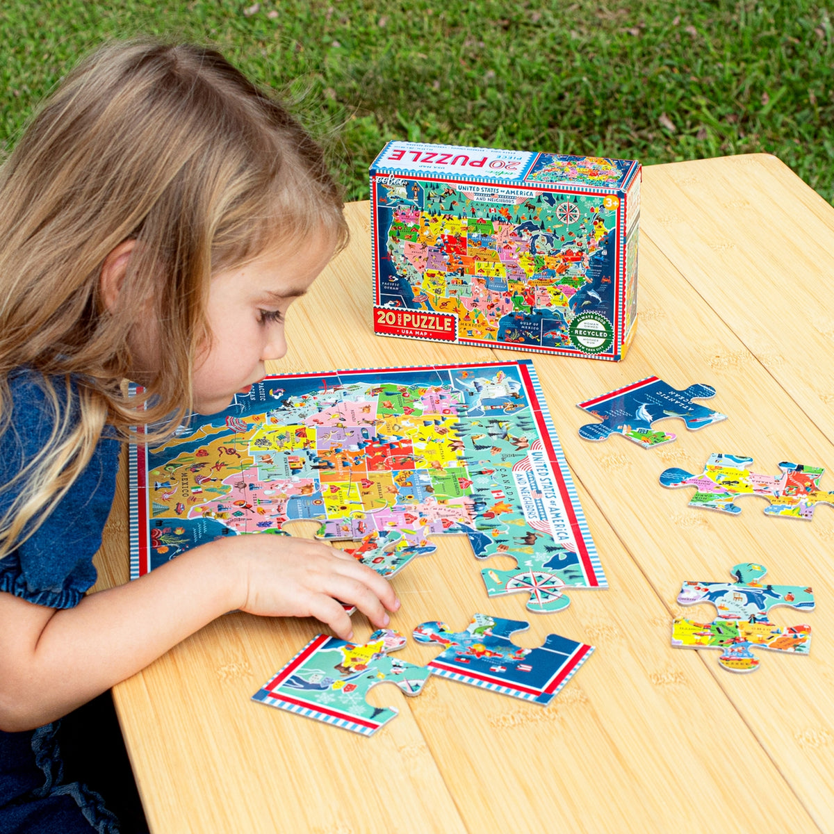 Child playing with a puzzle of the United States on a wooden table outdoors.