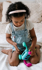 An infant sitting upright on a bed, playing with the Knudll Sensory Activity Toy by Mobi Games.